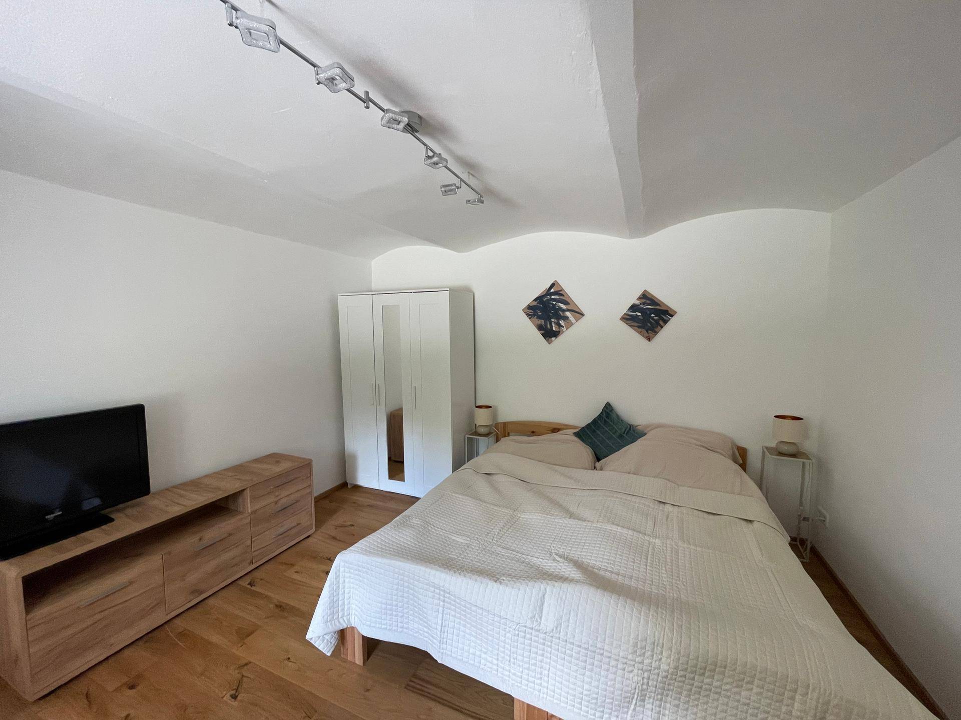 Schlafzimmer mit Doppelbett, Kleiderschrank, TV-Möbel und gewölbter Decke.
