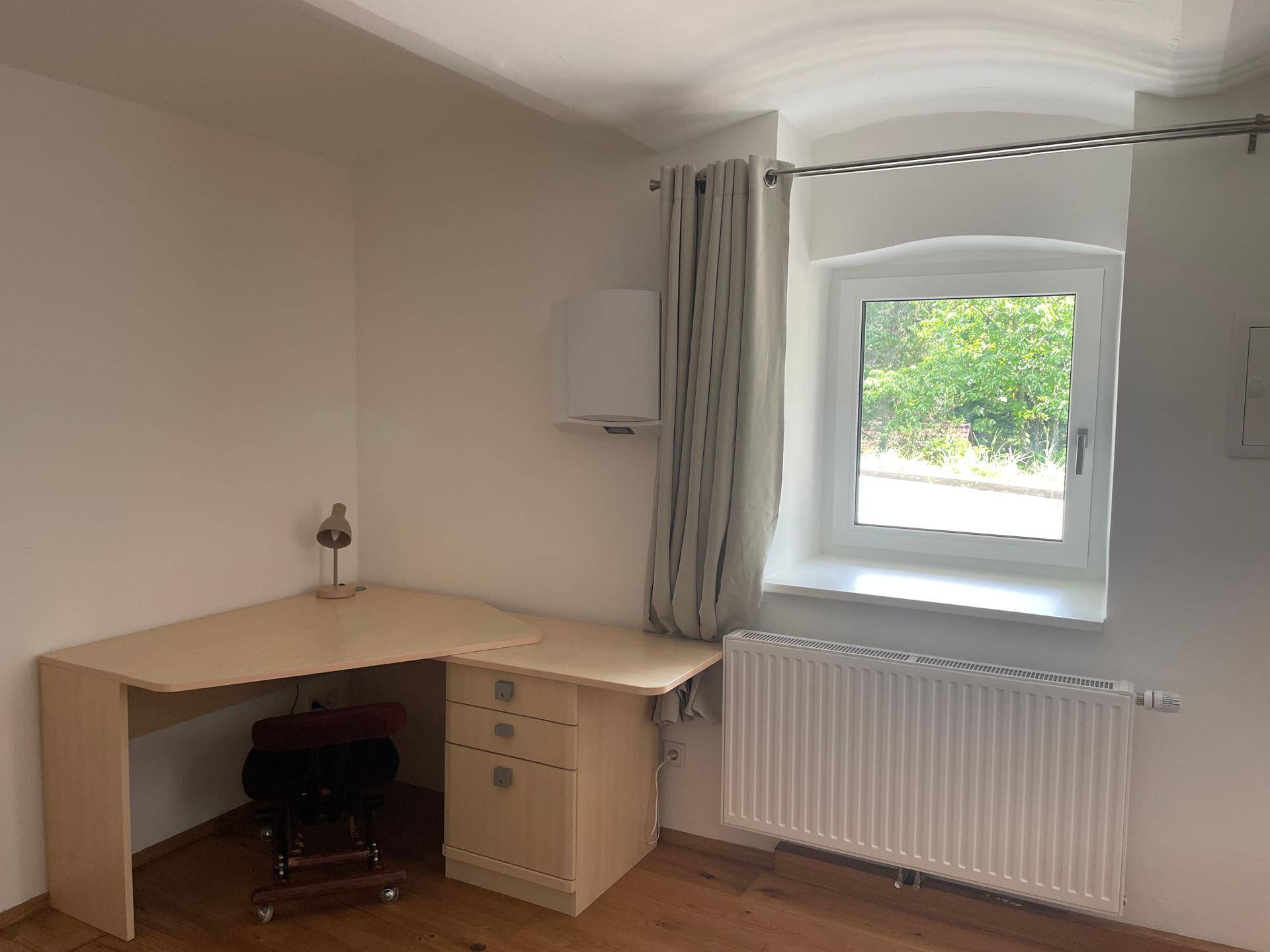 Helles Arbeitszimmer mit Eckschreibtisch und Fenster mit Blick ins Grüne.