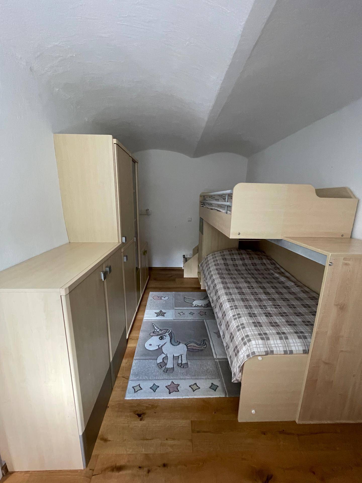 Kinderzimmer mit Etagenbett, hellen Holzmöbeln und einem verspielten Teppich.