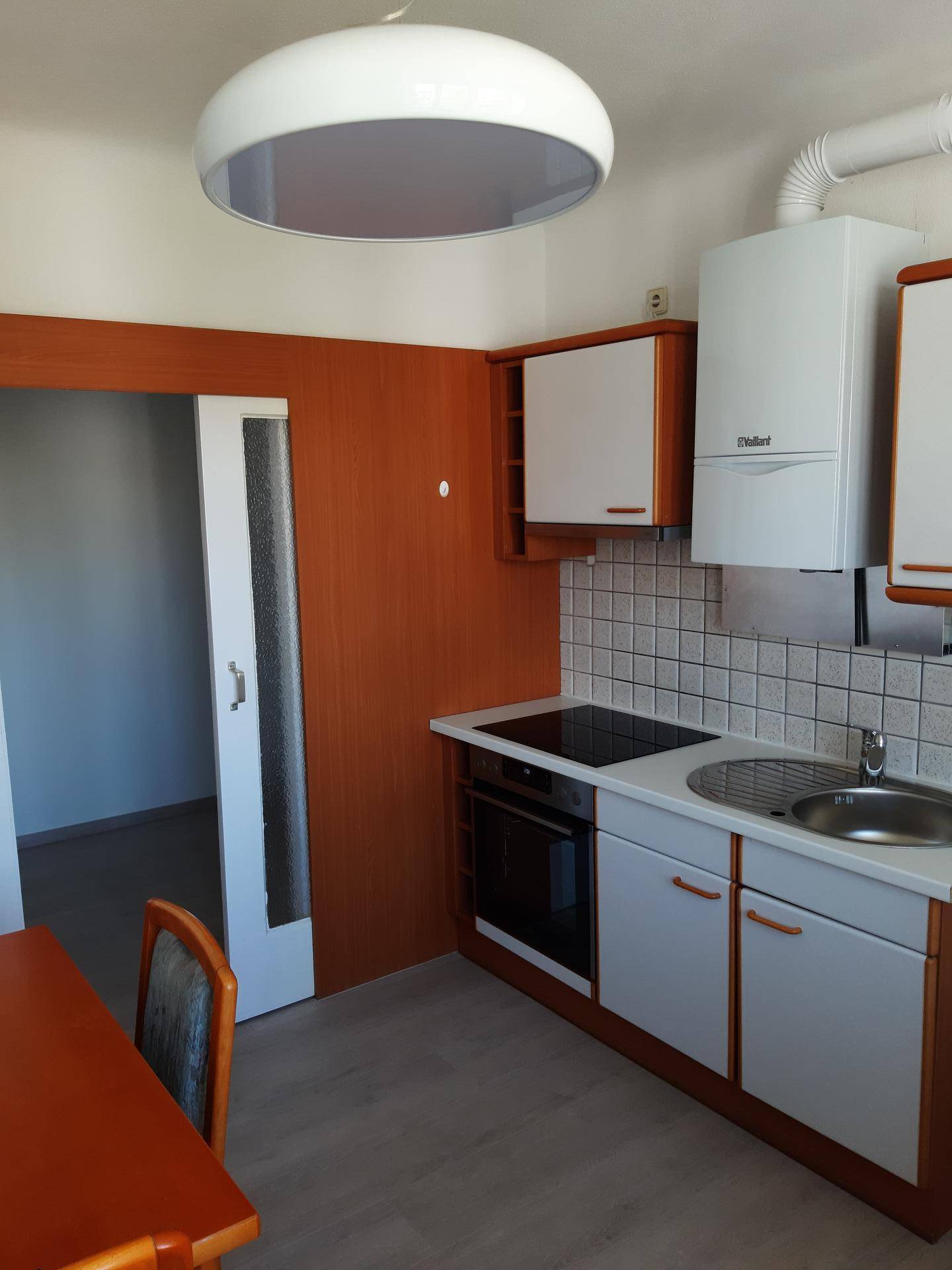 Funktionale Küche mit Induktionskochfeld, Backofen, Spüle und Wandheizkessel.