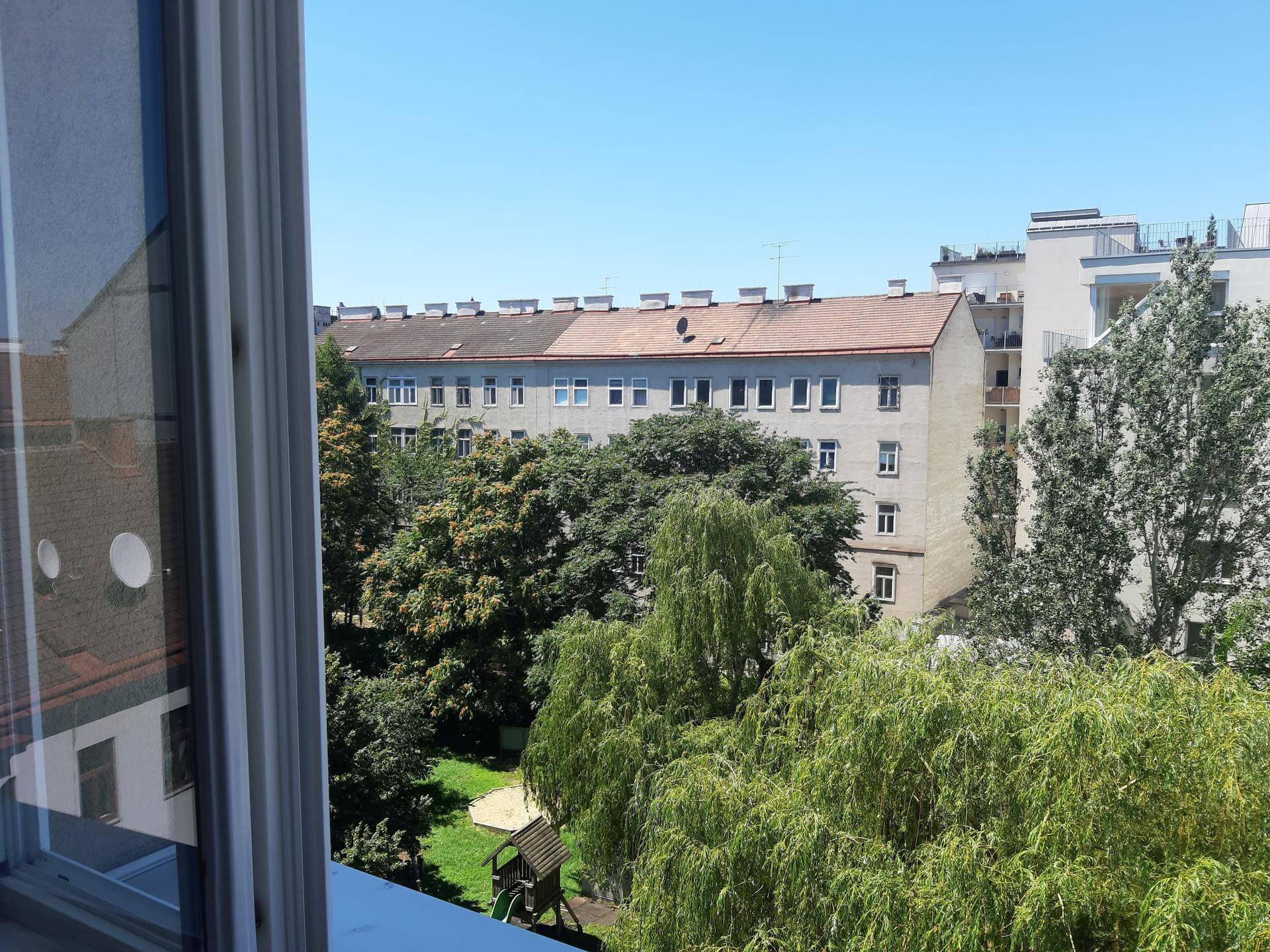 Blick aus dem Fenster auf einen grünen Innenhof mit Bäumen und einem Kinderspielplatz.