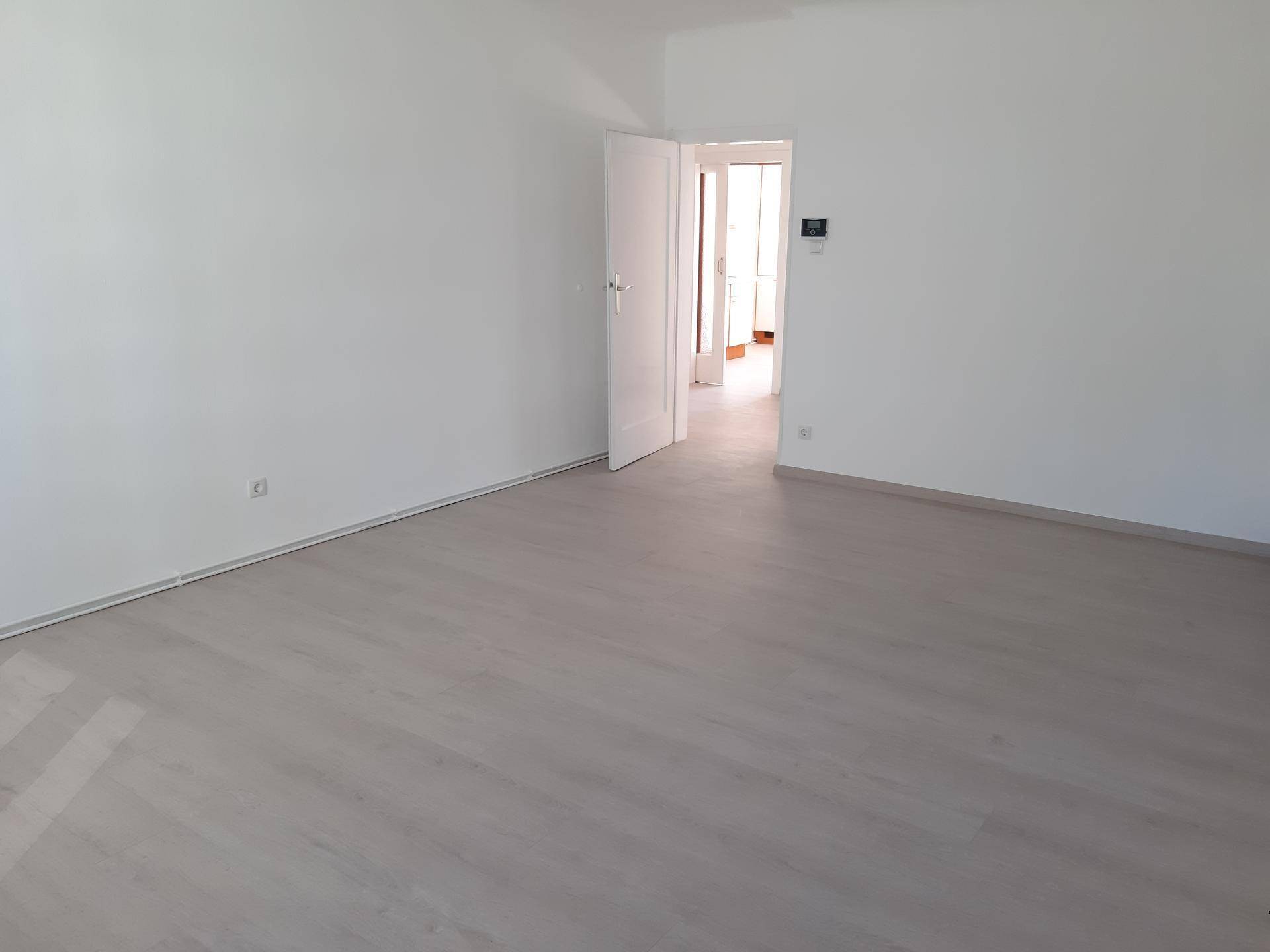 Leeres, helles Zimmer mit weiß gestrichenen Wänden und hellem Laminatboden.