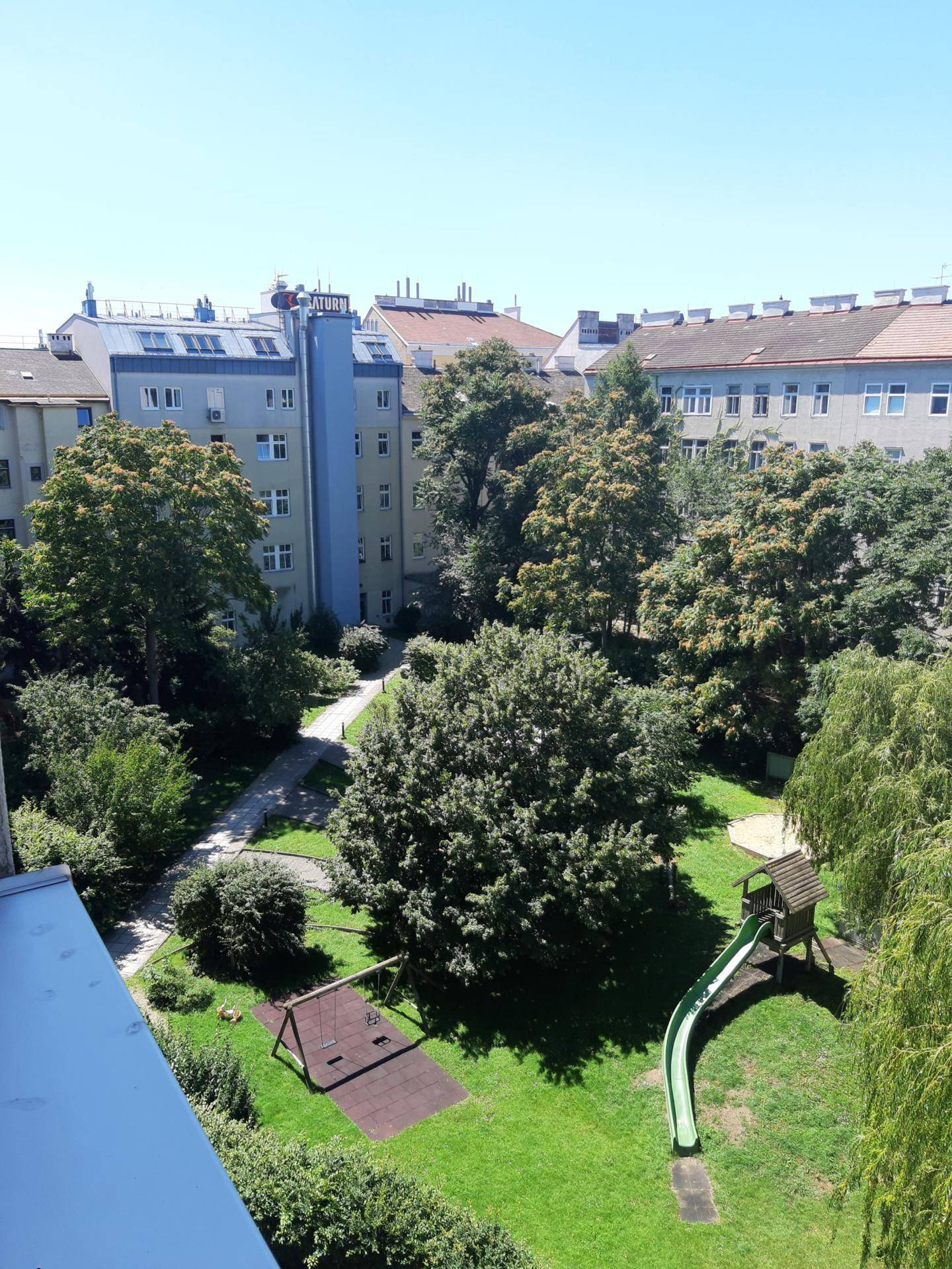 Weitläufiger Blick auf den grünen Innenhof mit Spielplatz, Bäumen und umliegenden Wohngebäuden.