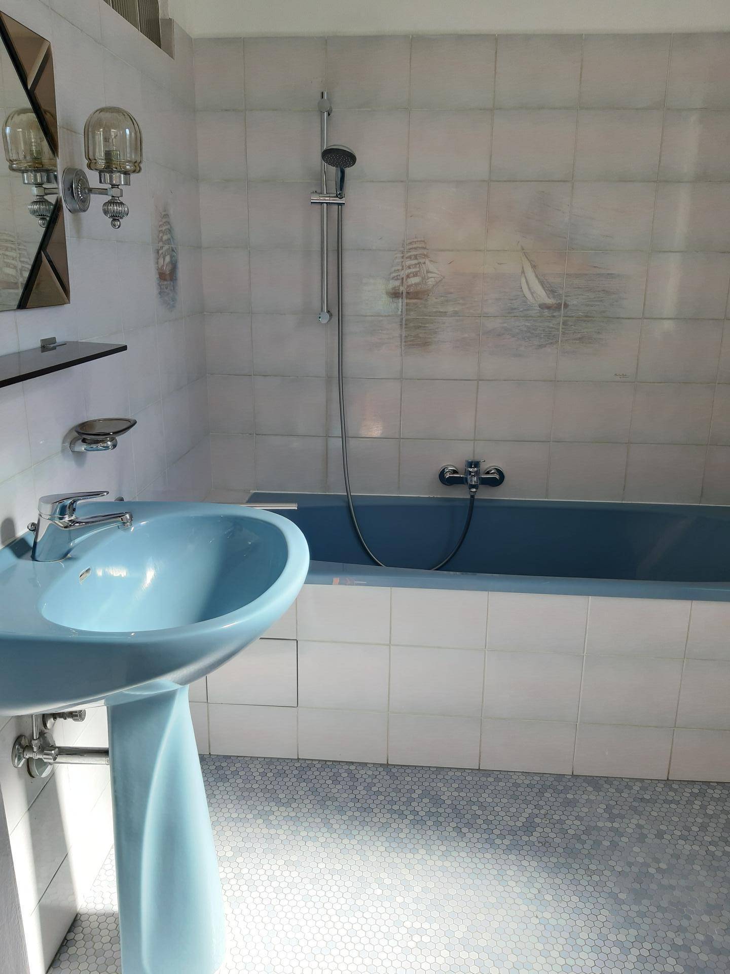Badezimmer mit blauer Badewanne und Waschbecken, weißen Fliesen und Duschvorrichtung.