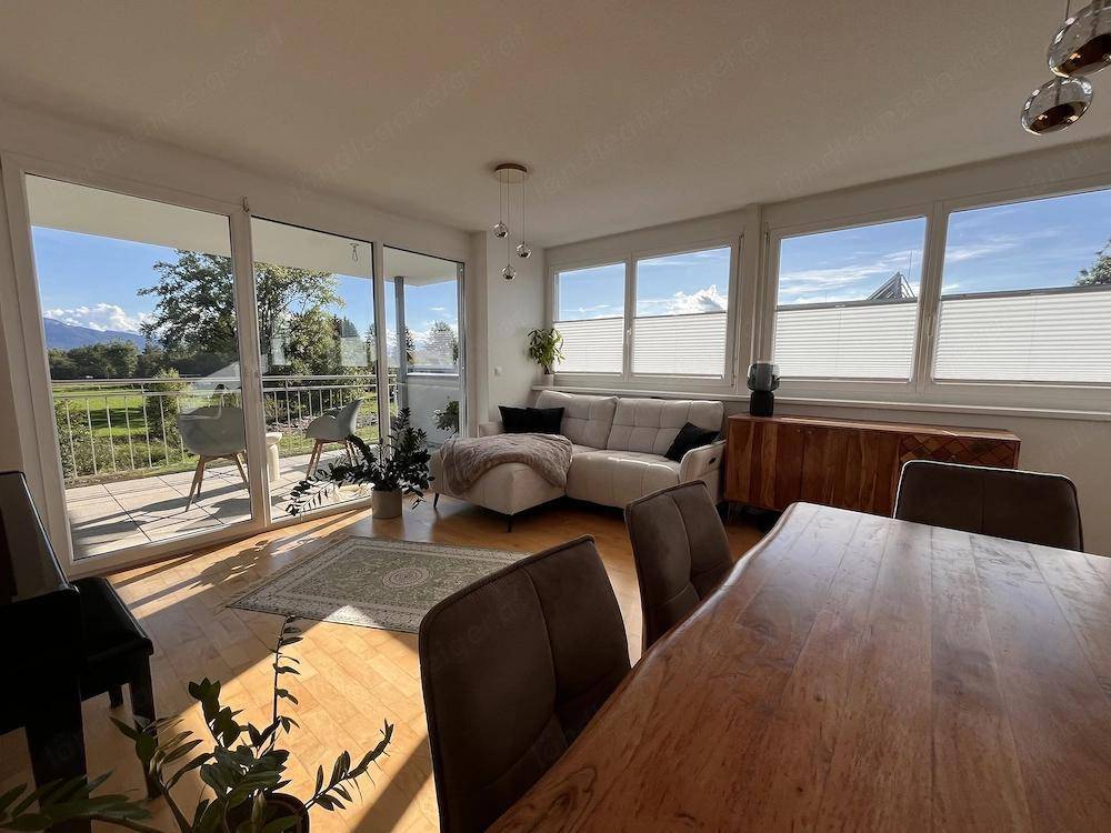 Heller Wohn- und Essbereich mit Holzboden, Zugang zum Balkon und weitem Blick ins Grüne.