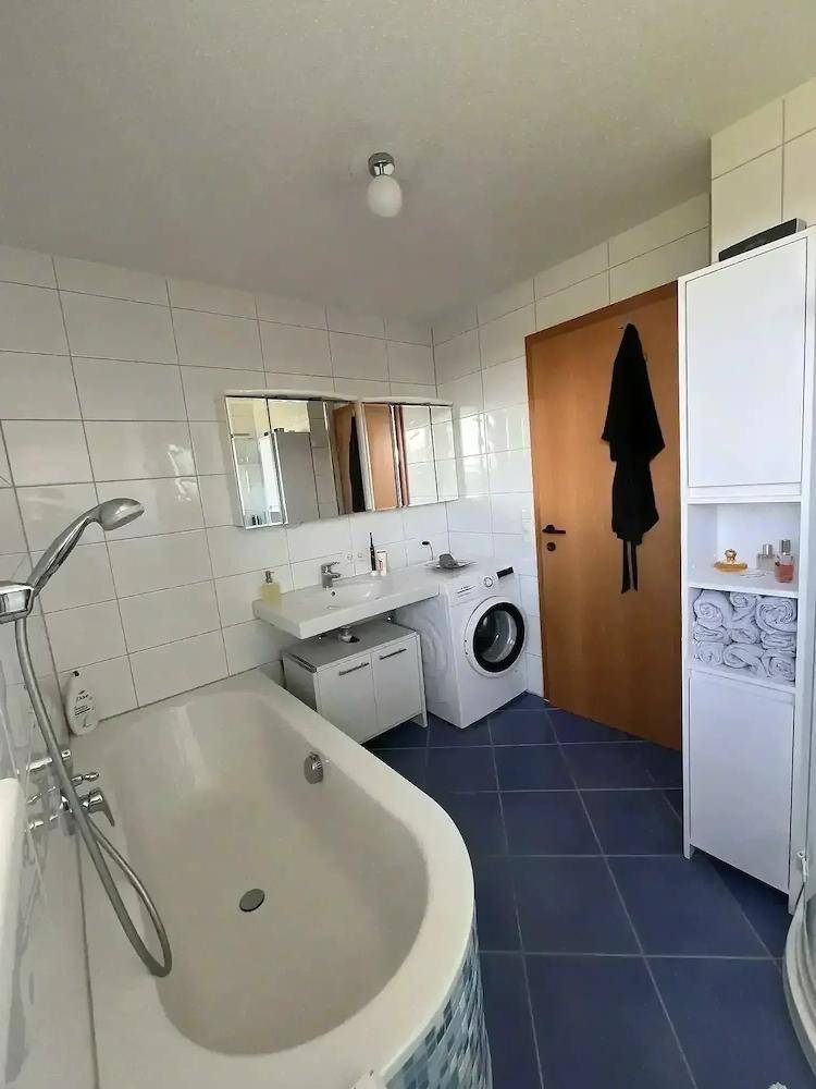 Funktionales Badezimmer mit Badewanne, Doppelwaschbecken, Waschmaschine und blauen Bodenfliesen.