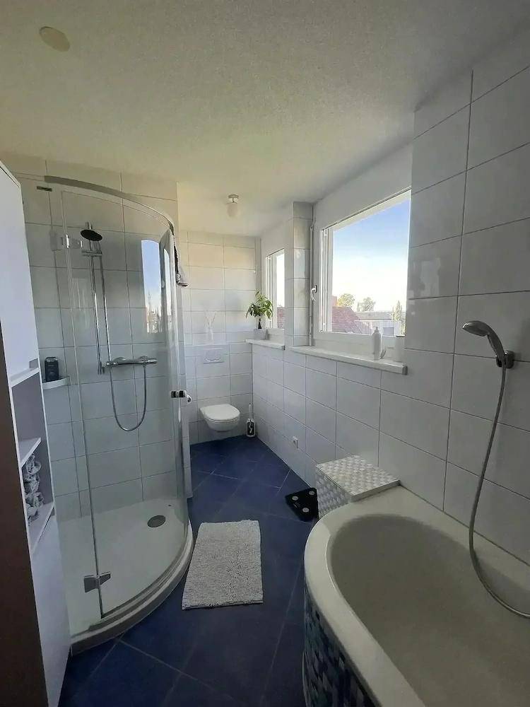 Modernes Badezimmer mit ebenerdiger Dusche, WC, Fenster und blauen Bodenfliesen.