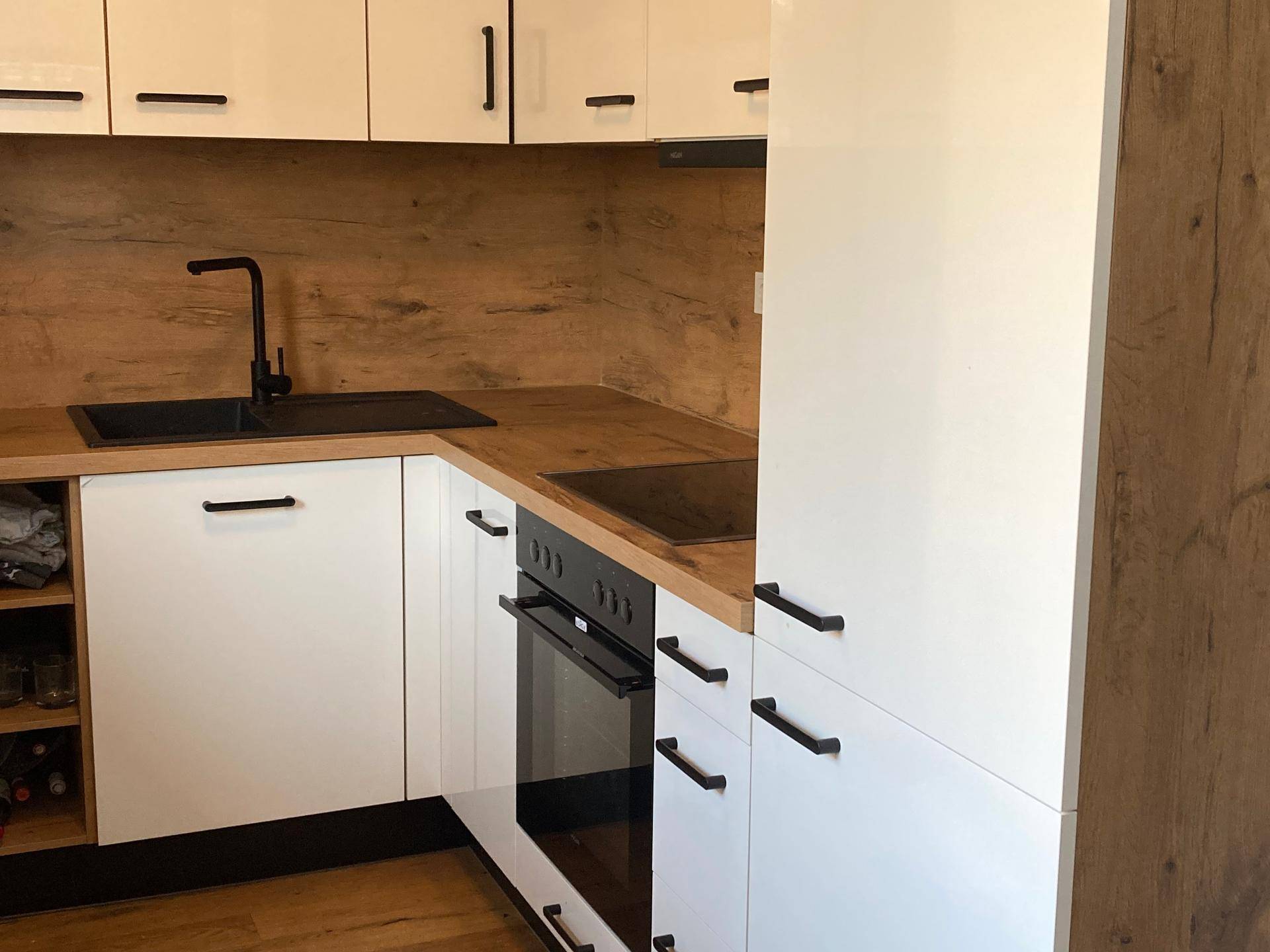 Moderne Küche mit weißen Hochglanzschränken, Holzarbeitsplatte und integriertem Backofen.