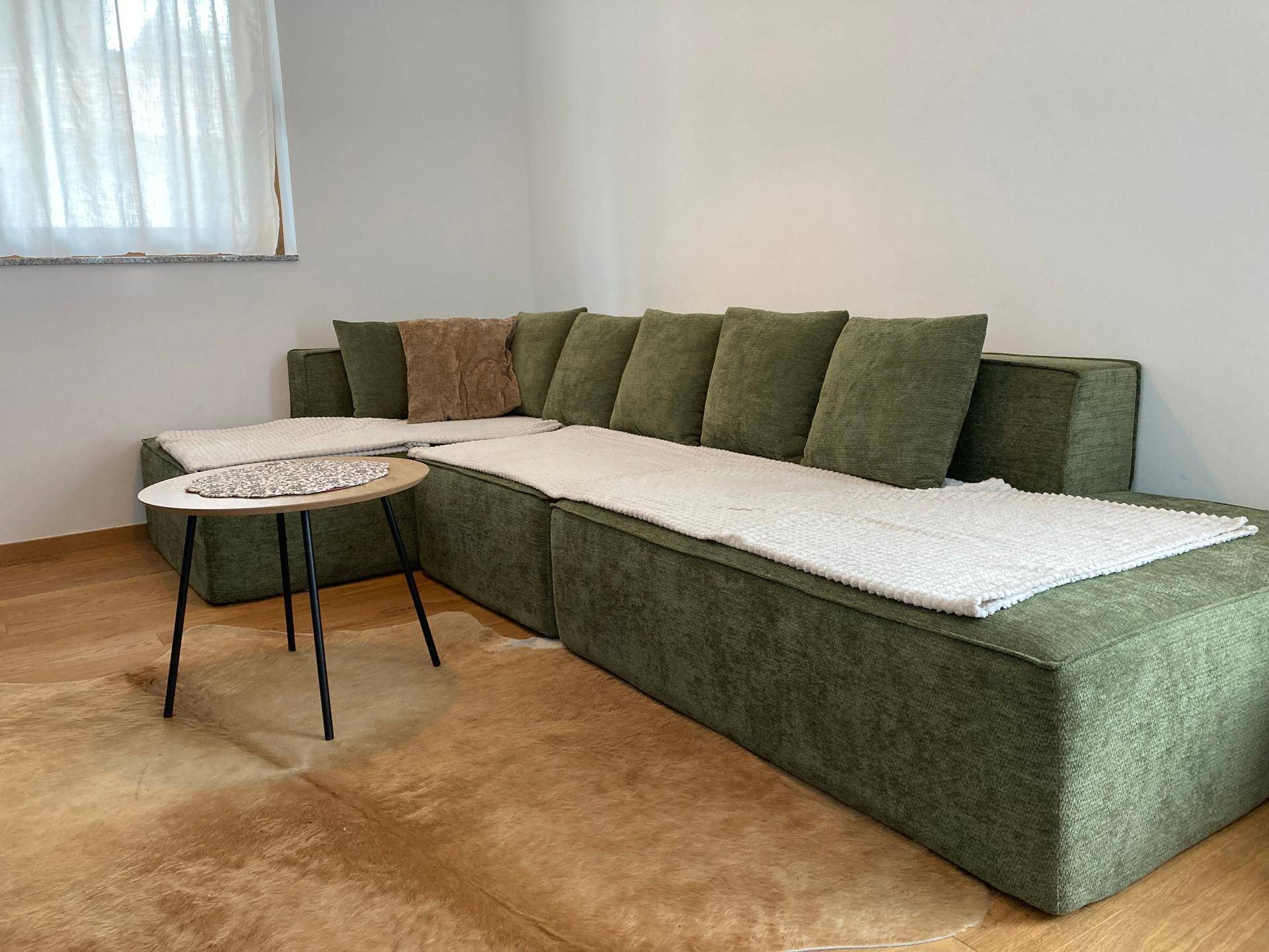 Gemütliches Wohnzimmer mit großem grünem Ecksofa, kleinem Couchtisch und Fenster.