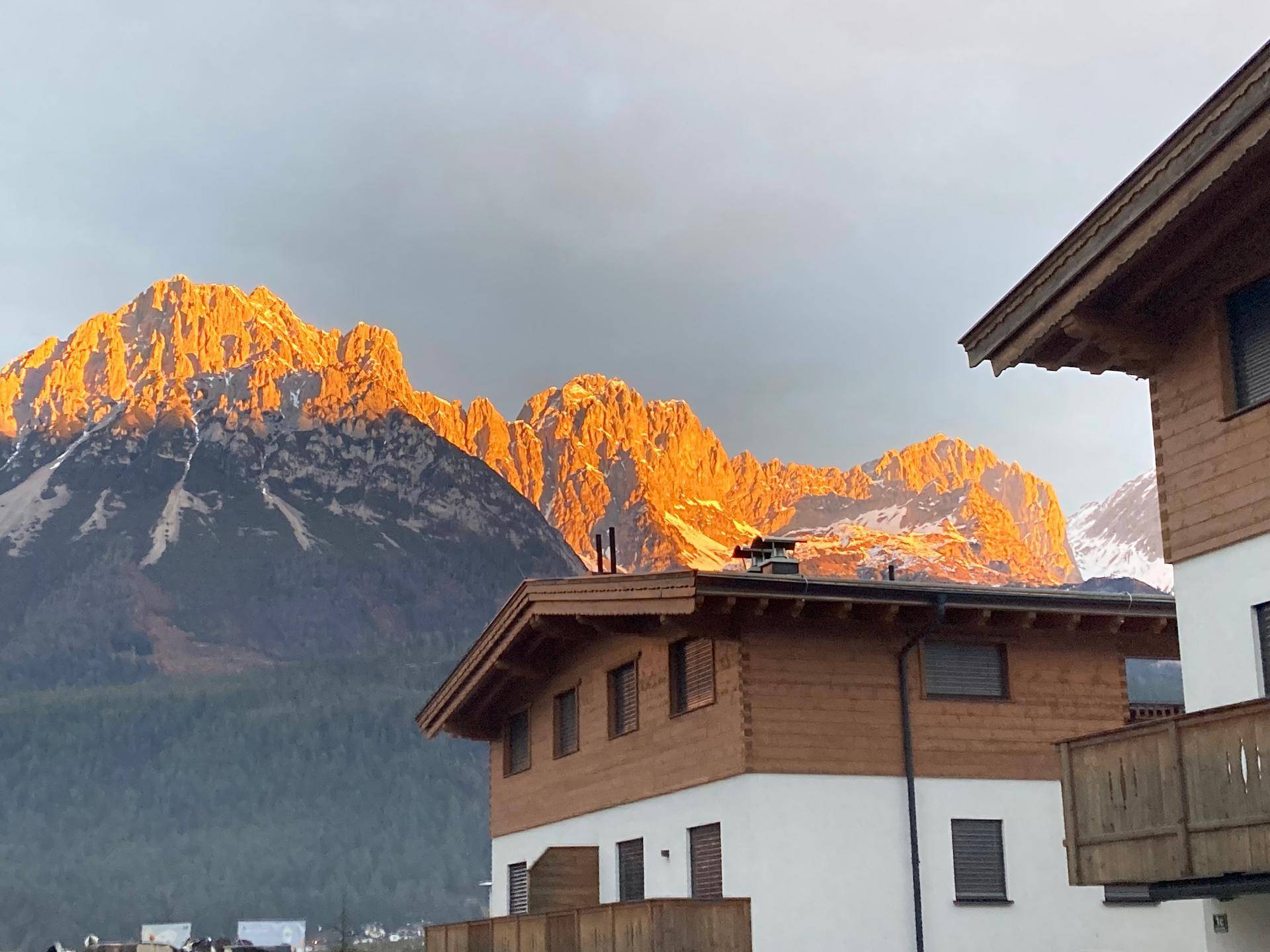 Gebäude mit traditioneller Holzfassade vor einer beeindruckenden, sonnenbeschienenen Bergkulisse.