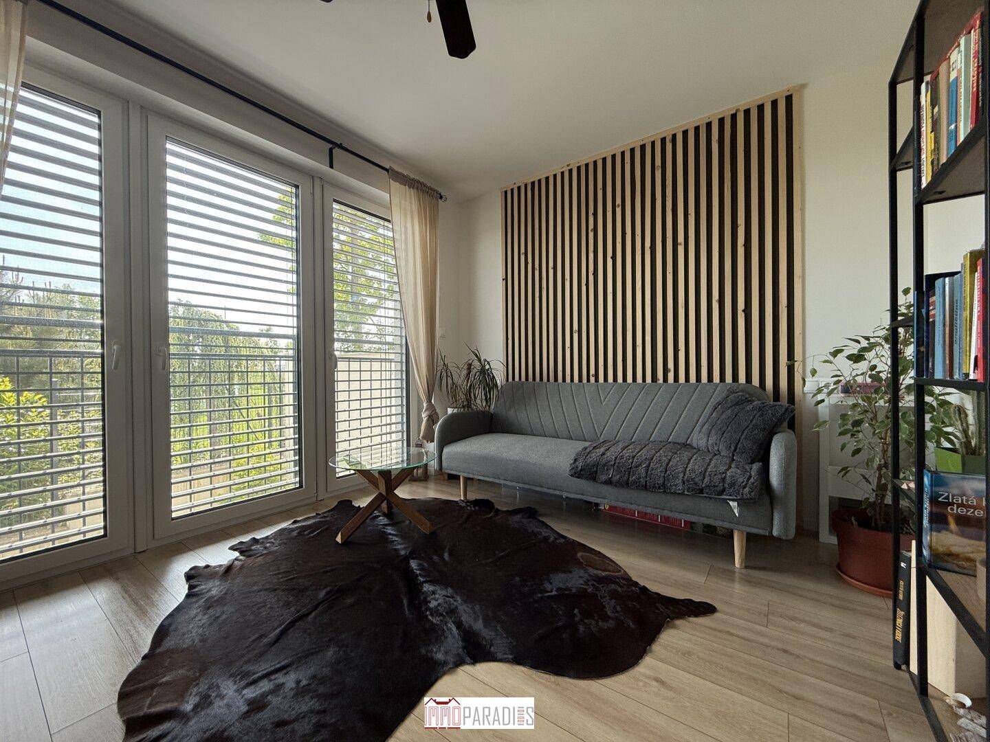 Helles Zimmer mit großzügigen Fenstern, Holzboden und modernem Sofa.