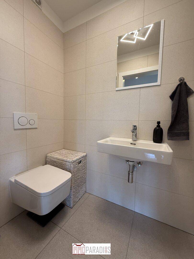 Modernes Gäste-WC mit wandhängender Toilette, Waschbecken und hellen Fliesen.