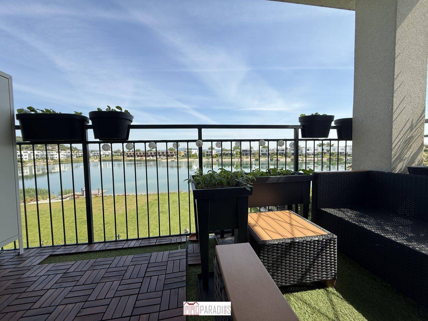 Balkon mit Seeblick, Outdoor-Möbeln und Pflanzen in Töpfen.