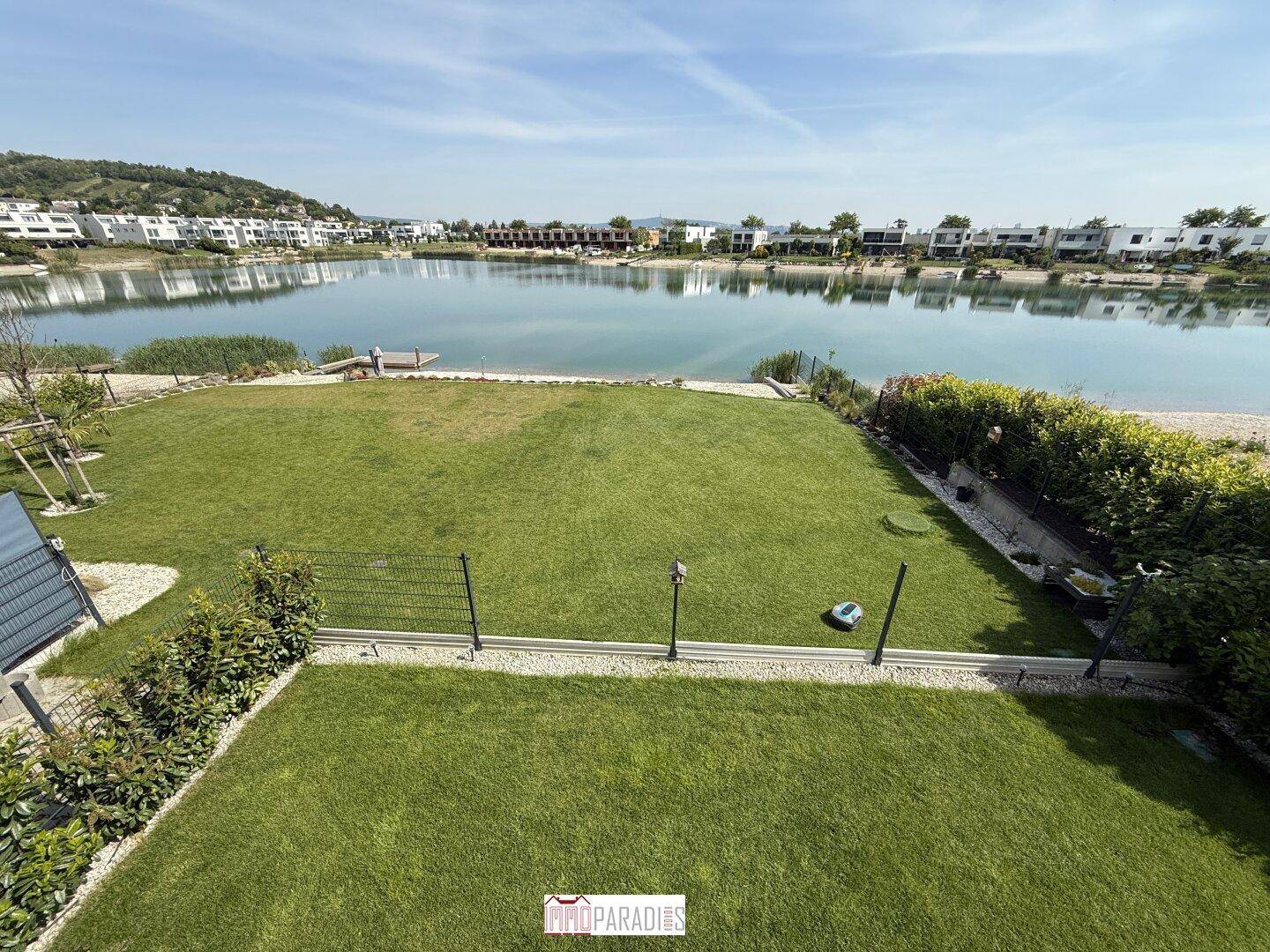 Großer, gepflegter Gartenbereich mit Rasen und Seeblick, umgeben von Hecken.