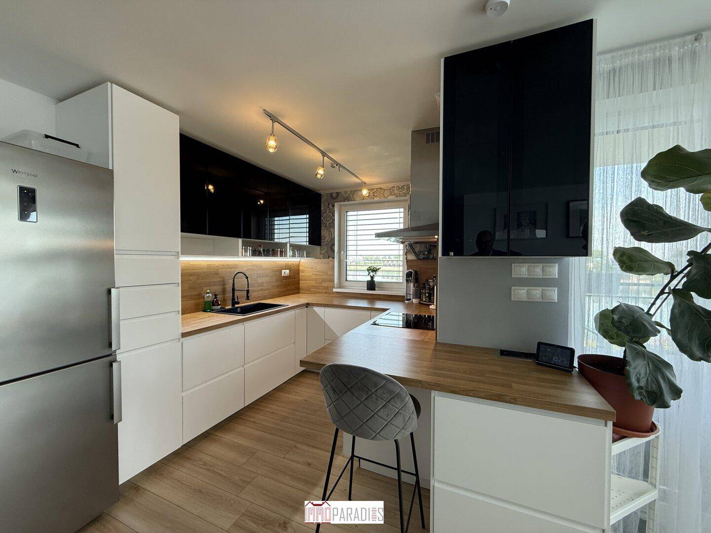 Moderne Küche mit weißen Unterschränken, Holz-Arbeitsplatte und schwarzen Oberschränken.