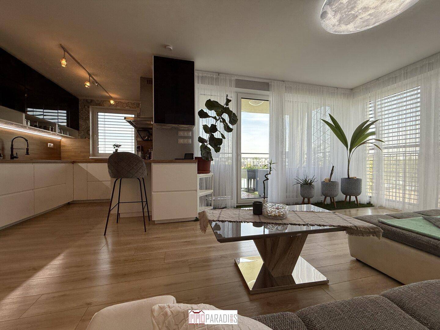 Offener Wohnbereich mit integrierter Küche, Holzboden und Zugang zum Balkon.