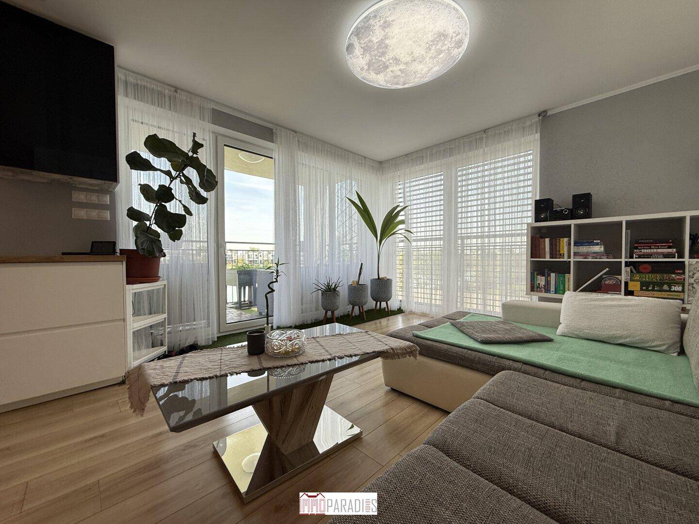 Helles Wohnzimmer mit großzügigen Fenstern, Holzboden und modernem Sofa.