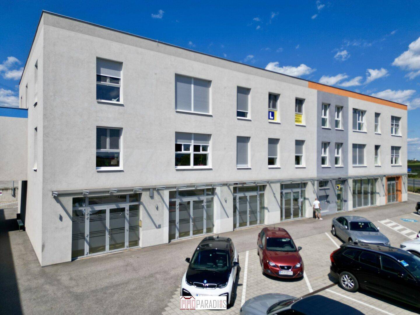 Modernes Geschäftsgebäude mit mehreren Etagen und großen Fenstern, umgeben von Parkplätzen.
