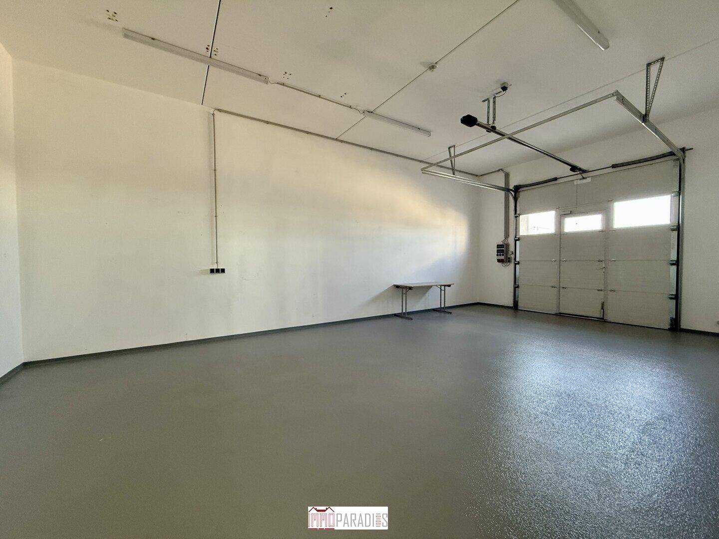 Geräumige Garage mit Rolltor und grauem Boden, ideal für Lagerung oder Fahrzeuge.
