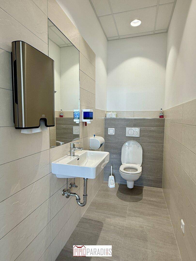 Modernes WC mit wandhängender Toilette, Waschbecken und großem Spiegel in neutralen Farben.
