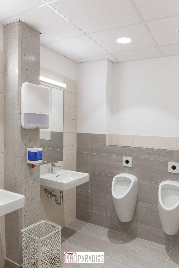 Moderner Herrenwaschraum mit zwei Urinalen, Waschbecken und hellen Fliesen an den Wänden.