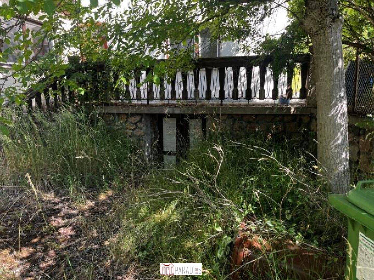 Überwachsener Balkon mit Steinbrüstung und Blick auf die umliegende Vegetation.