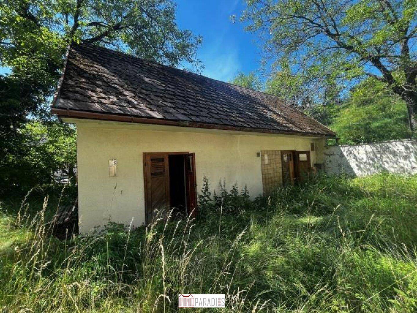 Kleines Nebengebäude oder Anbau mit Holztüren und einem verwilderten Gartenbereich.
