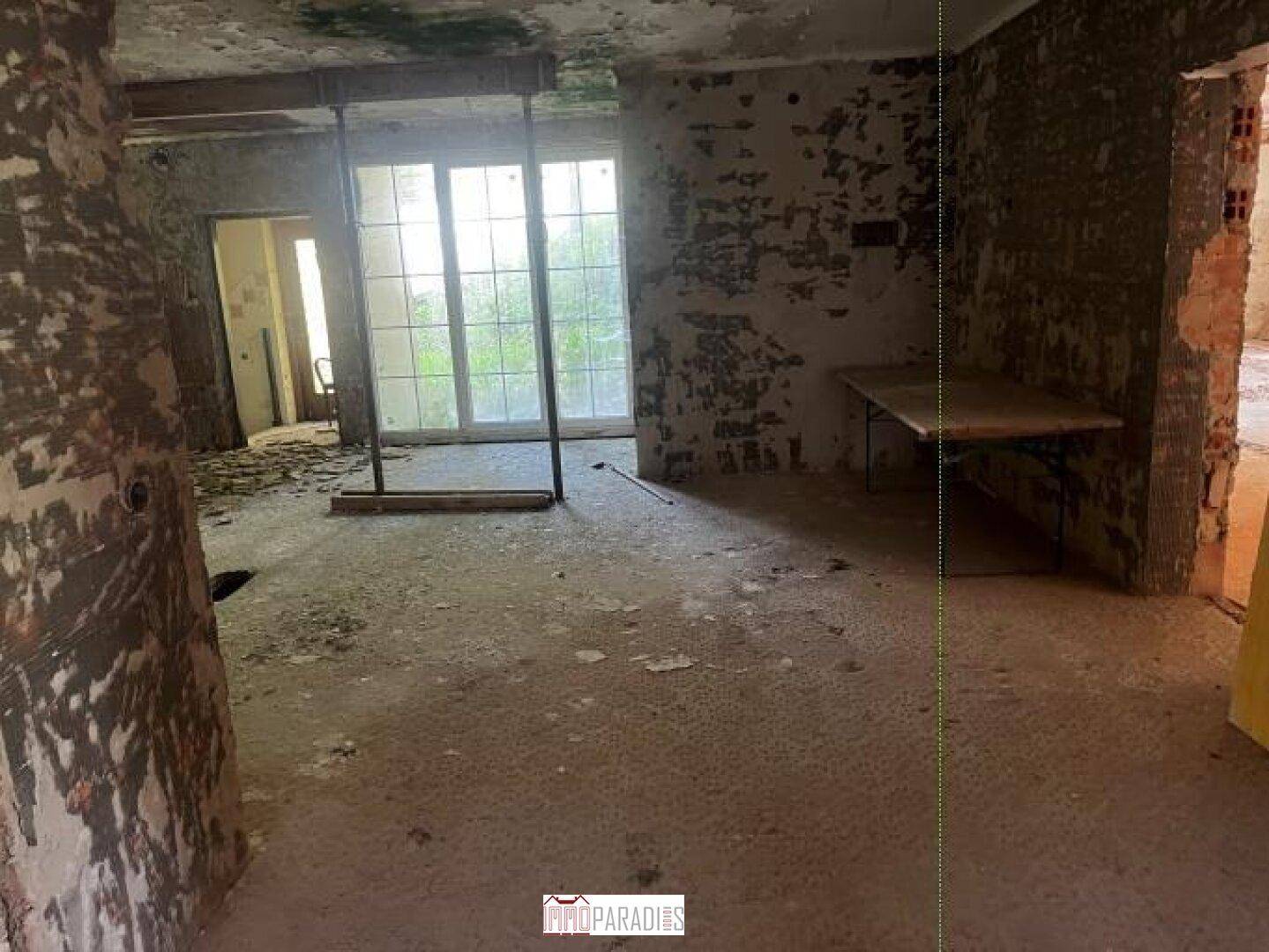 Unfertiger Raum mit großen Fensteröffnungen und Blick ins Grüne.