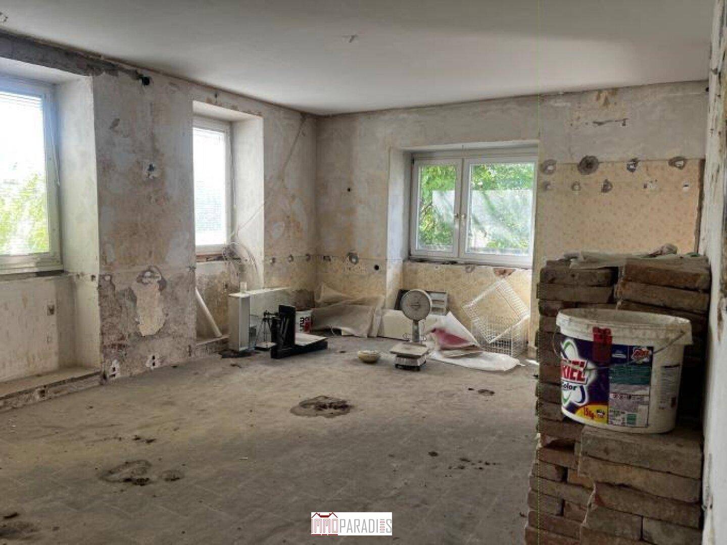 Unfertiger Raum mit Fenstern und verschiedenen Materialien für die Renovierung.