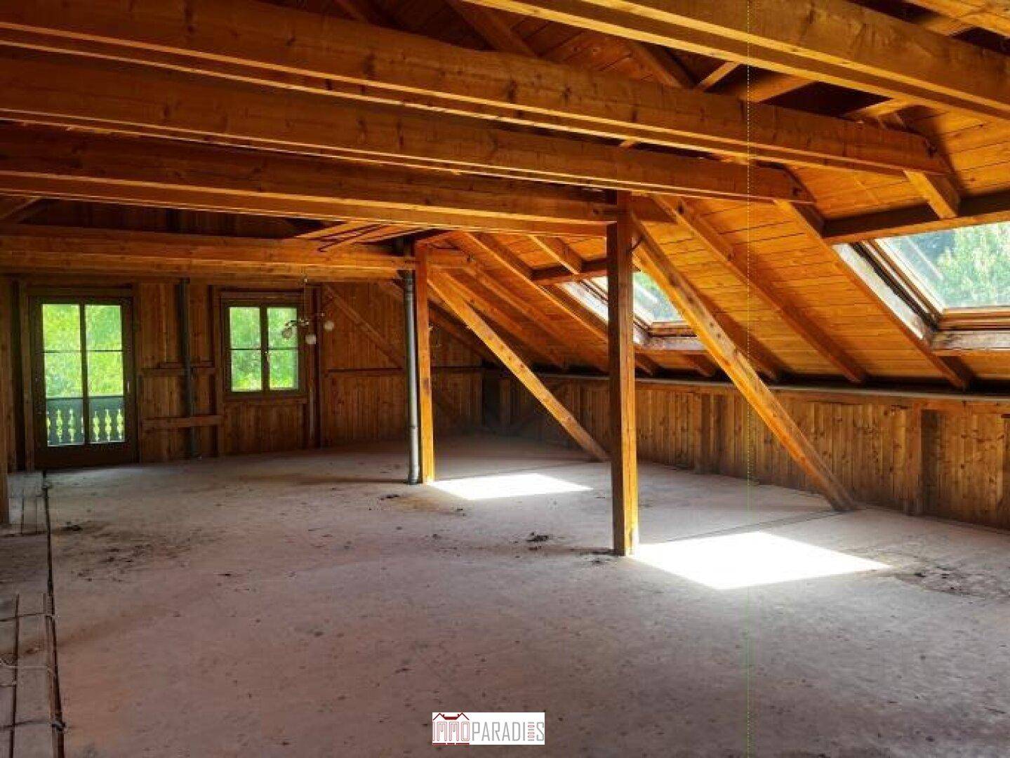 Unausgebauter Dachboden mit sichtbaren Holzbalken, Holzverkleidung und Dachfenstern.