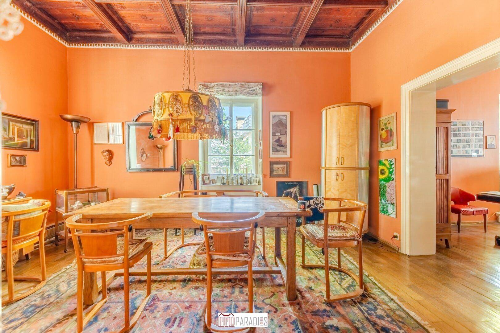 Traditionelles Esszimmer mit Holztisch, Stühlen und einer verzierten Holzdecke in warmen Farbtönen.