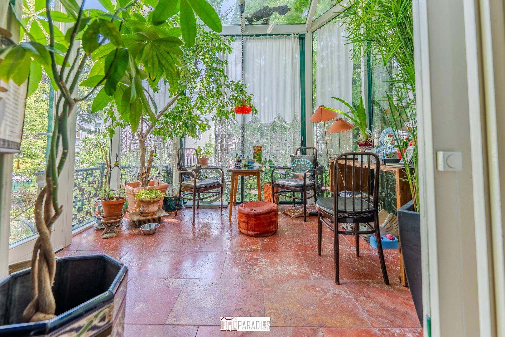 Heller Wintergarten mit Terrakotta-Bodenfliesen, vielen Pflanzen und gemütlichen Sitzgelegenheiten.