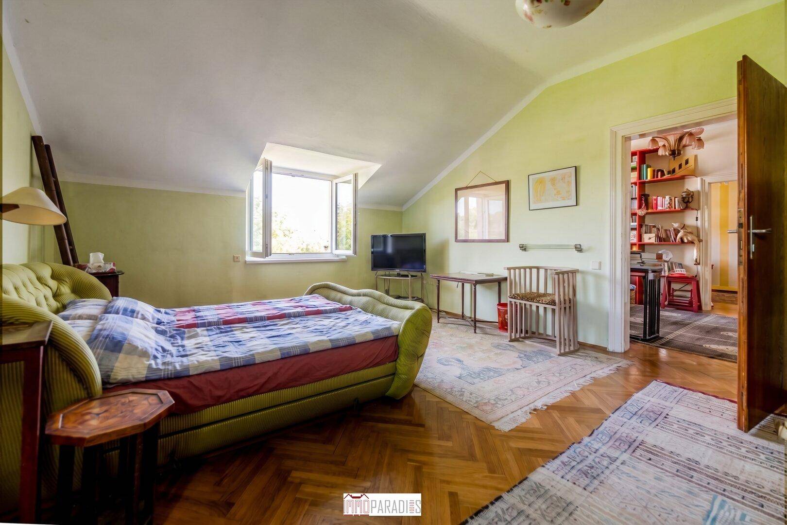 Gemütliches Schlafzimmer mit Dachschräge, Holzboden und einem Fenster mit Blick ins Grüne.
