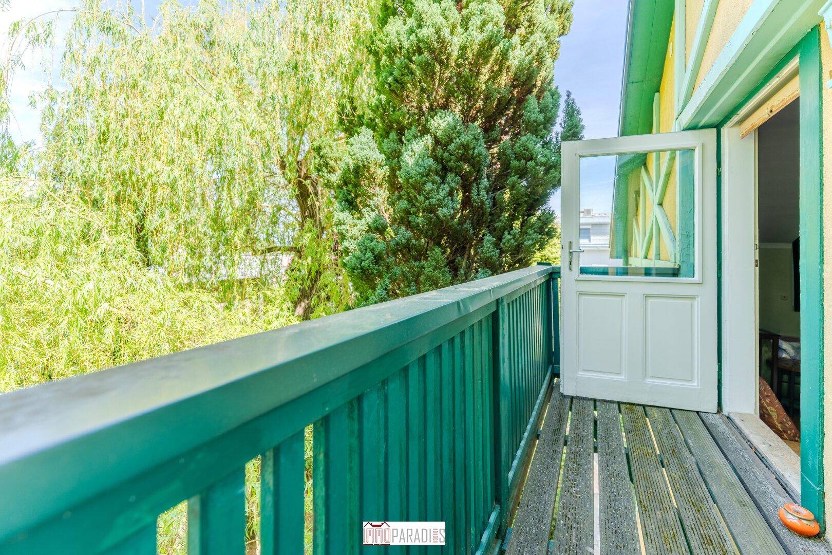Kleiner Balkon mit Holzgeländer und Blick auf üppige grüne Bäume, ideal zum Entspannen.