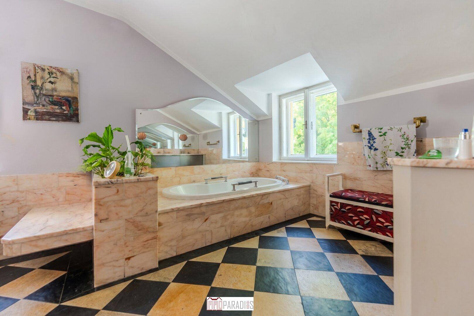 Geräumiges Badezimmer mit eingebauter Badewanne, Marmorverkleidung und Schachbrettmuster-Fliesenboden.
