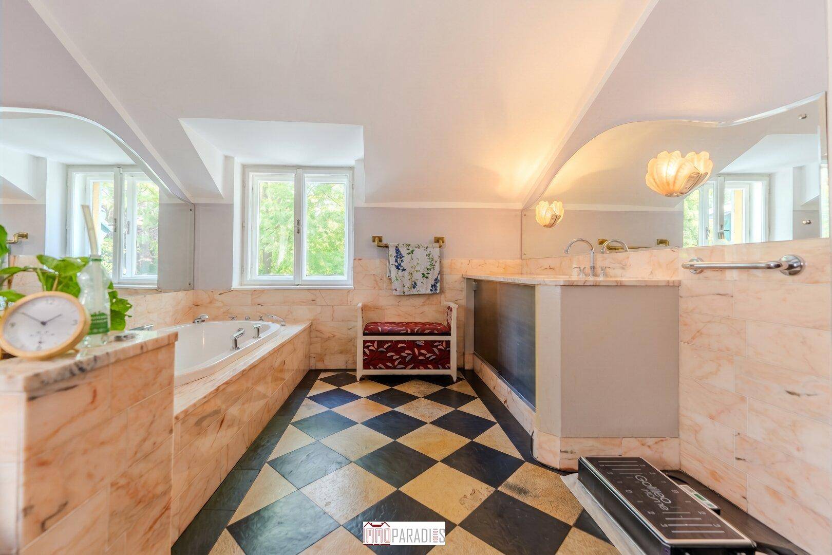 Elegantes Badezimmer mit Marmoroberflächen, großer Badewanne und einem Fenster für natürliches Licht.