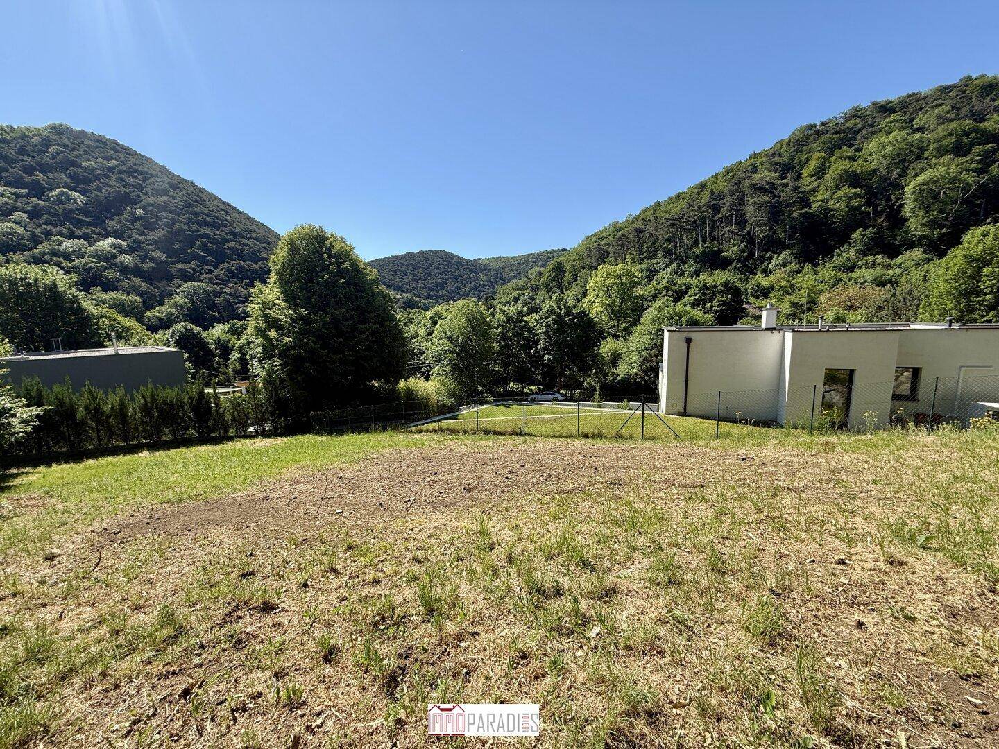 Offenes Grundstück mit Panoramablick auf bewaldete Hügel und ein modernes Gebäude.
