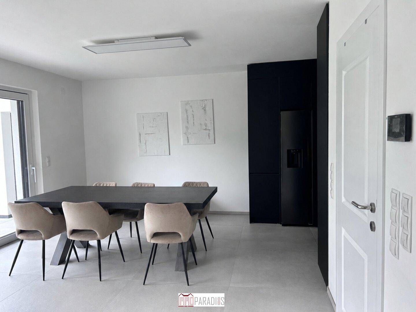 Moderner Essbereich mit großem dunklem Esstisch, beigen Stühlen und integriertem Kühlschrank.