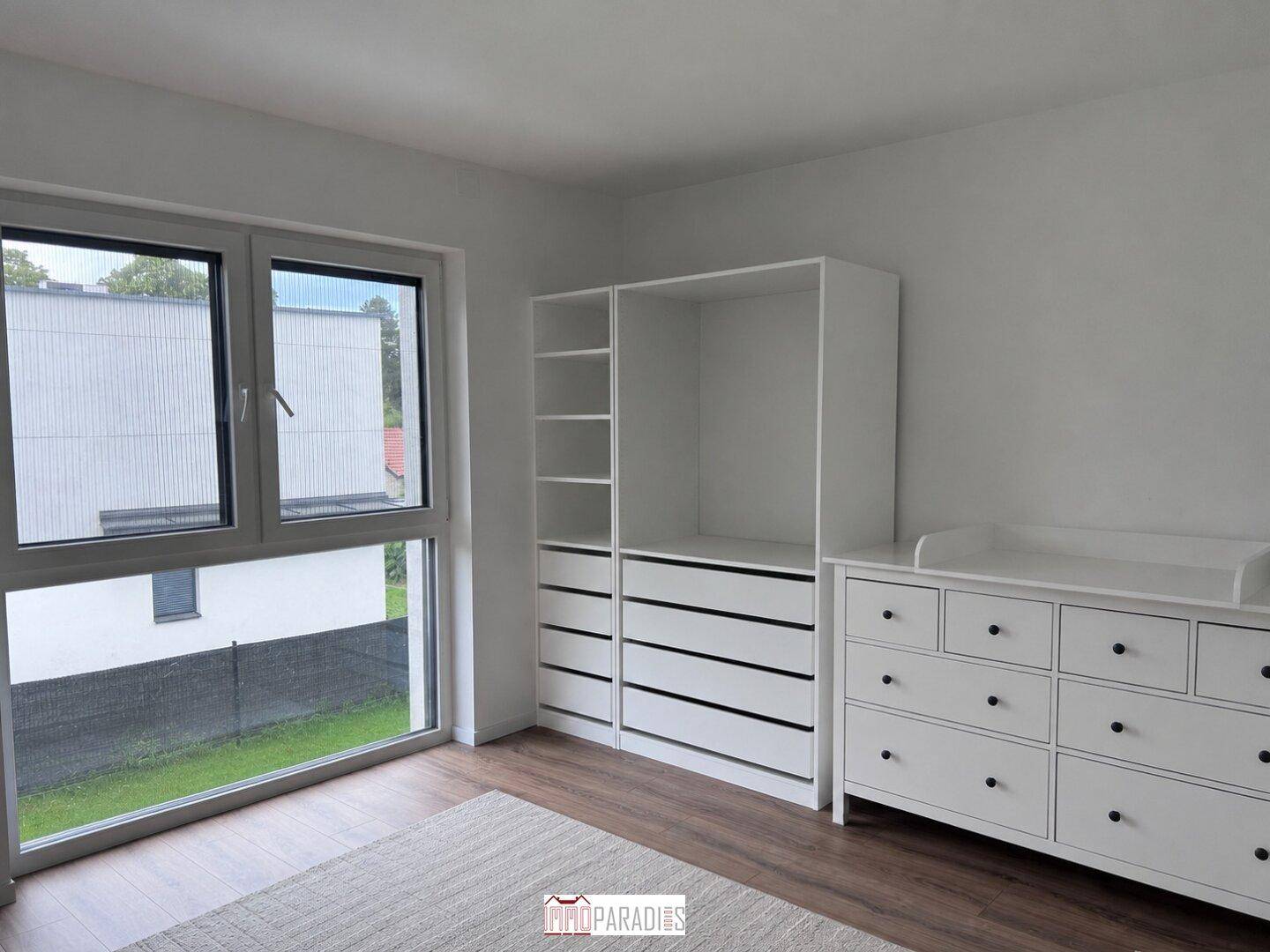 Helles Schlafzimmer mit großem Fenster, weißem Kleiderschrank und Wickelkommode.