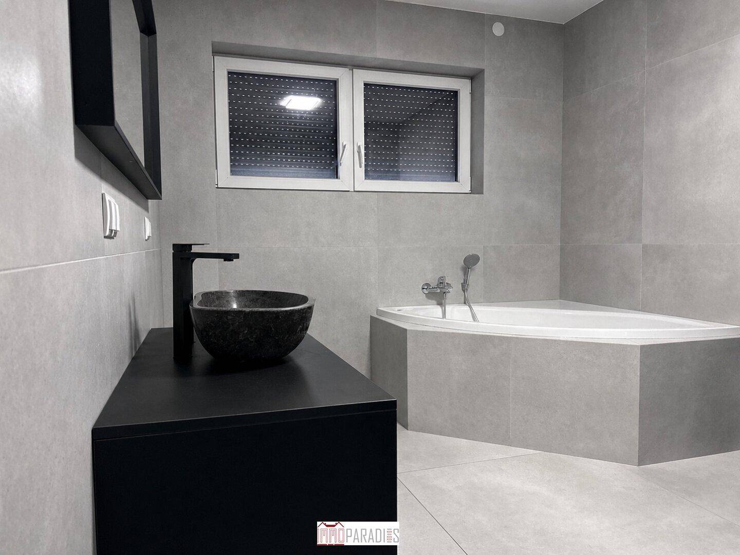 Modernes Badezimmer mit grauen Fliesen, schwarzem Waschtisch und Eckbadewanne.