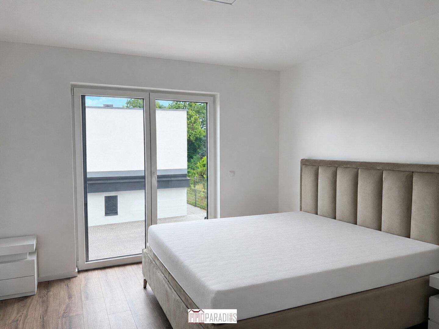 Helles Schlafzimmer mit großem Bett, Holzboden und Zugang zu einem Außenbereich.