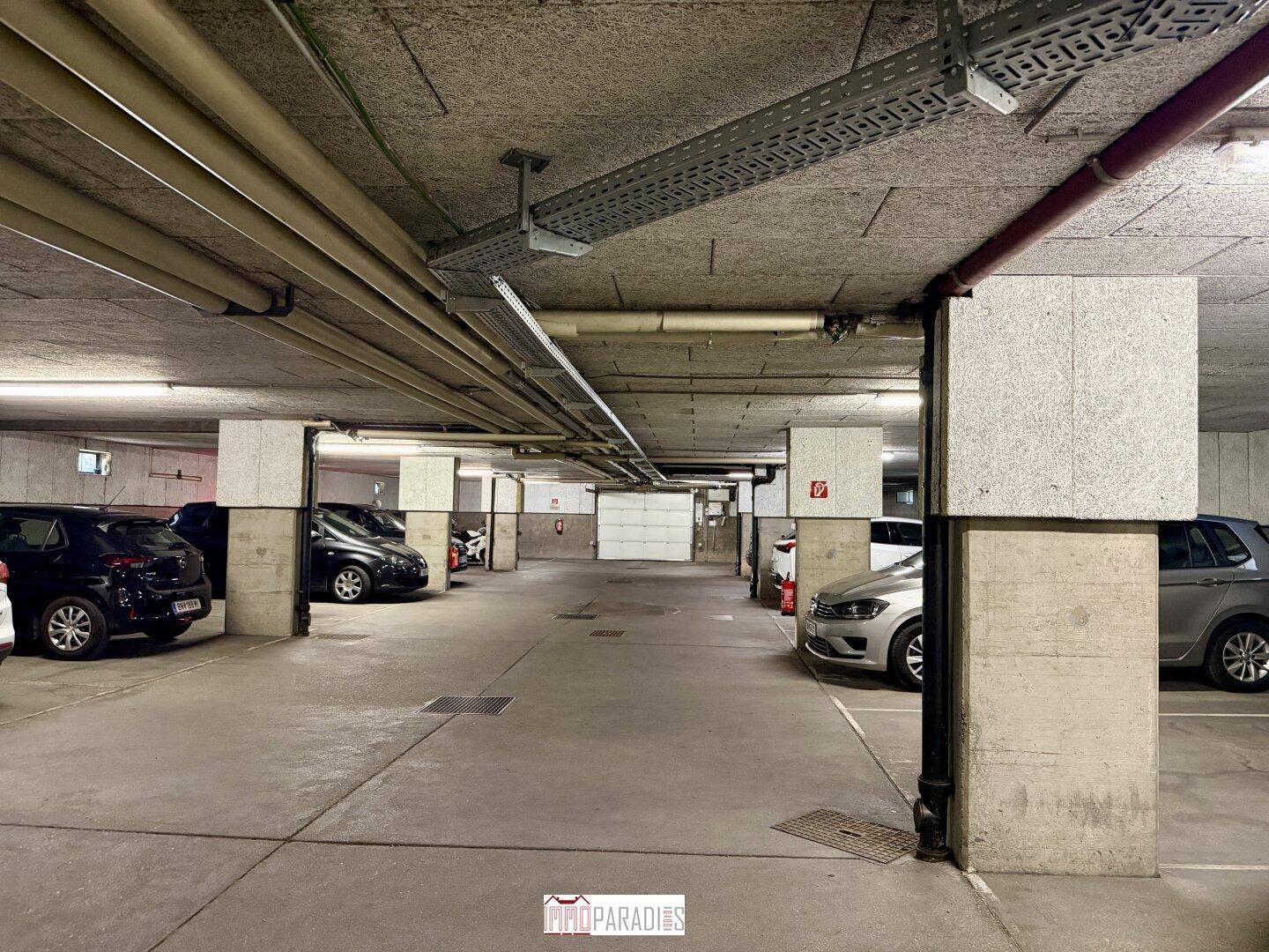 Tiefgarage mit mehreren Stellplätzen und sichtbaren Versorgungsleitungen an der Decke.