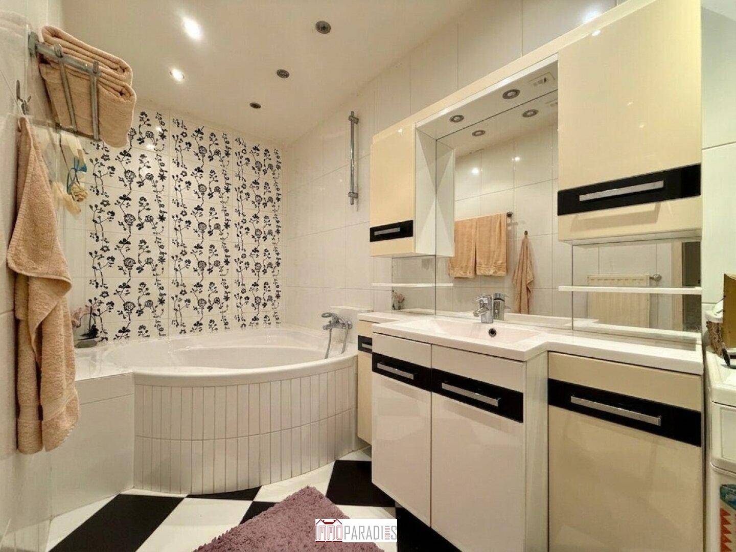Badezimmer mit Eckbadewanne, Waschbecken und Spiegel, dekoriert mit floraler Tapete.