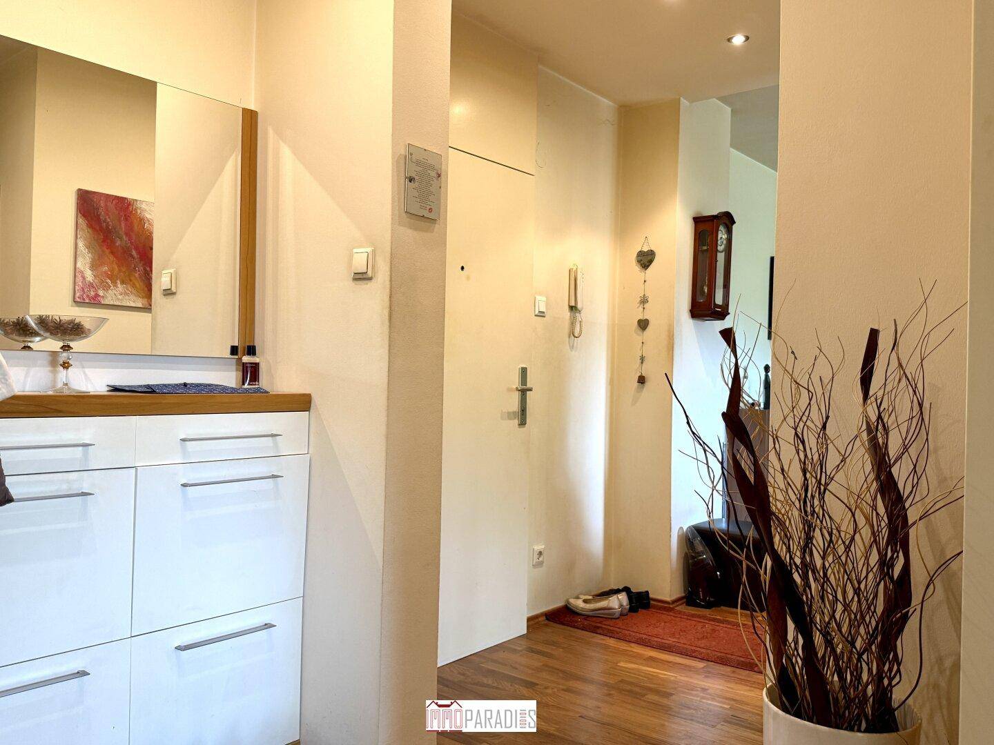 Heller Eingangsbereich mit Holzboden, Spiegel und Garderobe, der zu den Wohnräumen führt.