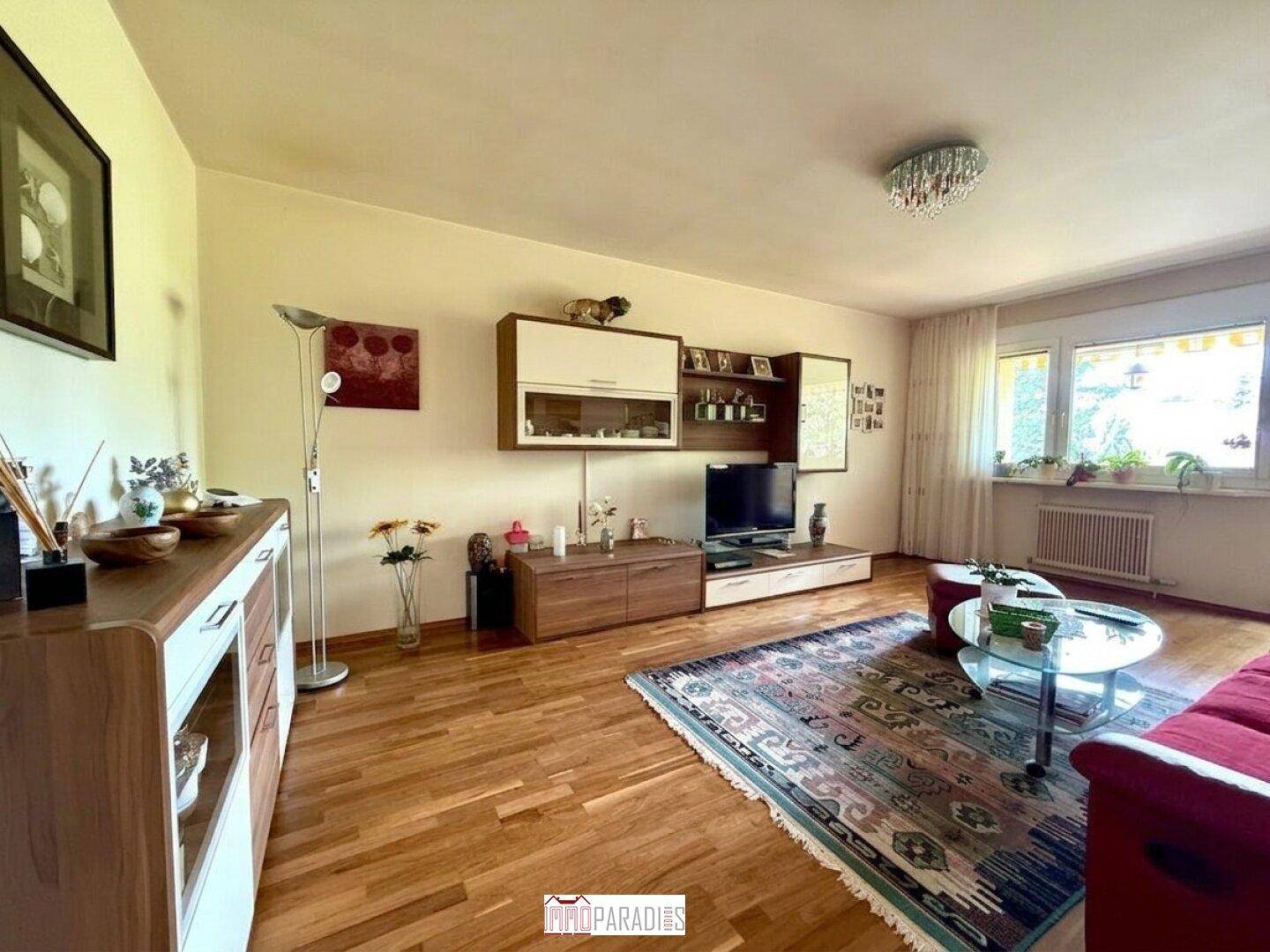 Helles Wohnzimmer mit Holzboden, großem Fenster und gemütlicher Sitzecke.