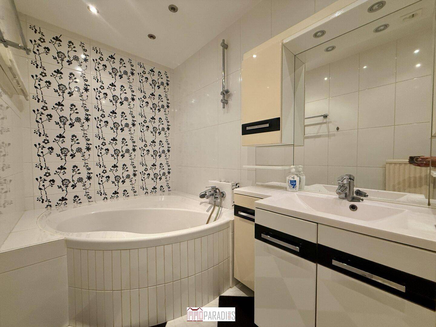 Badezimmer mit Eckbadewanne, floralen Wandfliesen und Spiegelschrank über dem Waschbecken.