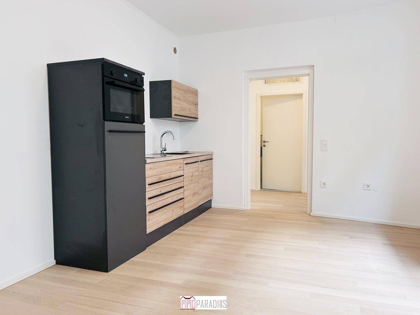 Moderne Küchenzeile mit schwarzen und holzfarbenen Schränken, integriertem Backofen und hellem Parkettboden.