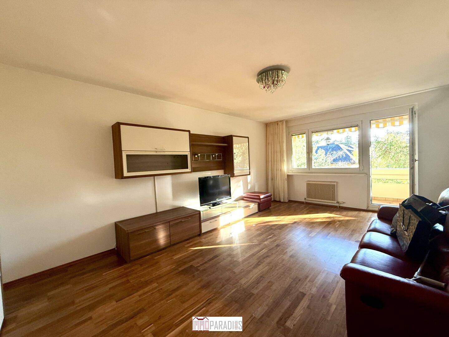 Helles Wohnzimmer mit Parkettboden, moderner TV-Wand und Zugang zum sonnigen Balkon.