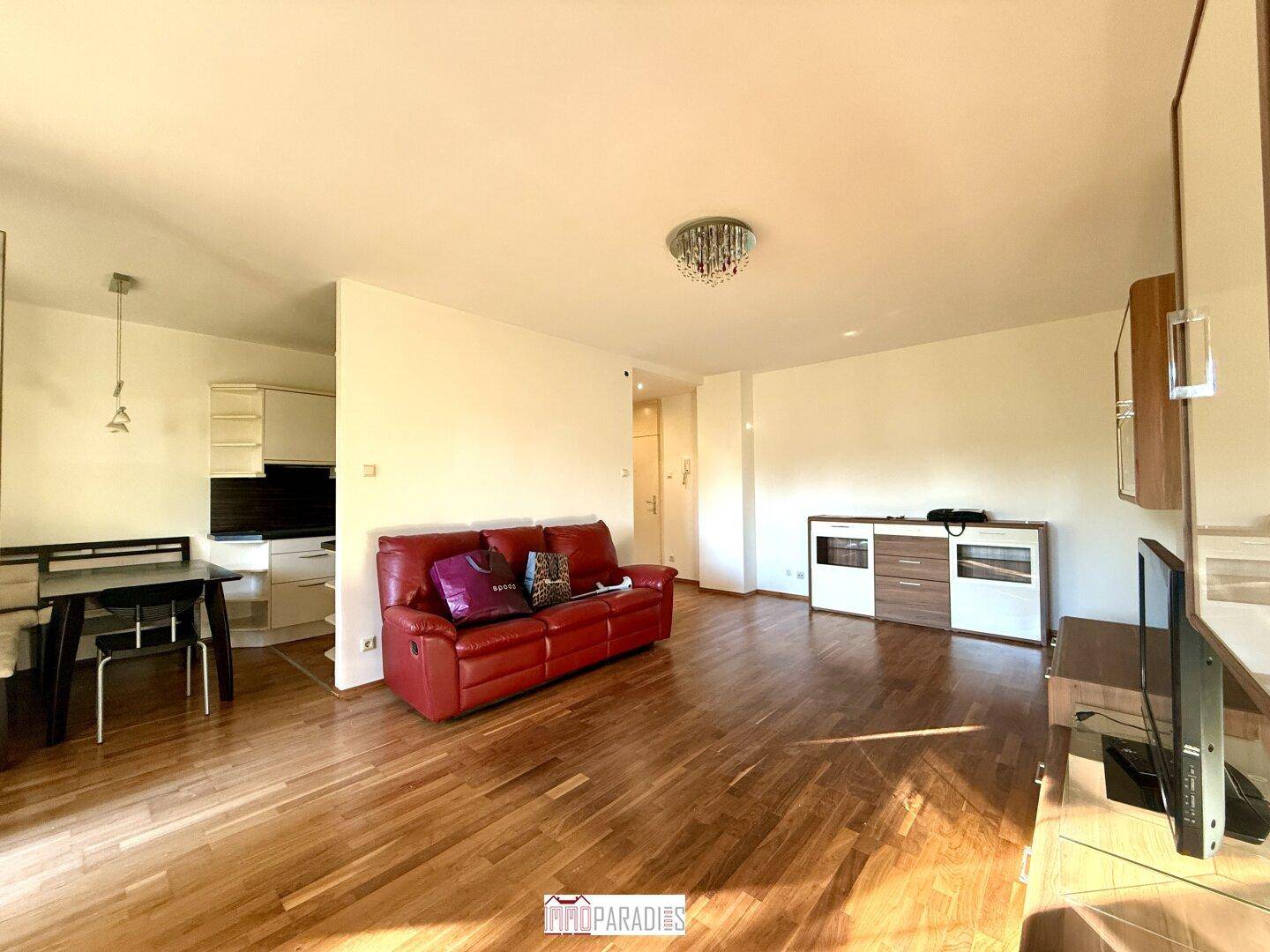 Offener Wohnbereich mit Parkettboden, rotem Sofa und Blick auf die angrenzende Küche.