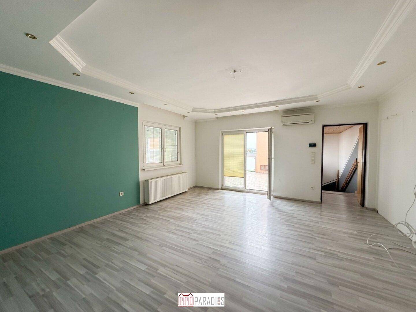 Helles Wohnzimmer mit Laminatboden, Klimaanlage und Zugang zu einem Balkon.